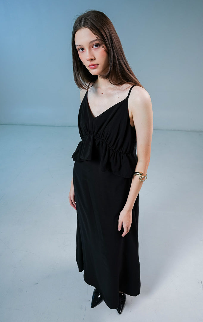 Model wanita mengenakan Haven V-Neck Ruffle Peplum Maxi Dress warna hitam, gaun panjang long dress wanita dengan detail kerut peplum dan tali spageti. 