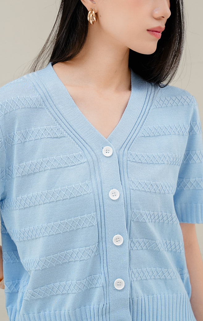Atasan rajut wanita warna biru muda Maysie Top dengan motif rajut geometris lattice, kerah V-neck, lengan pendek, dan kancing depan elegan. 