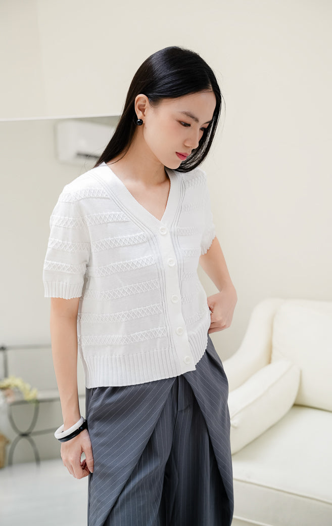 Atasan rajut wanita warna putih Maysie Top dengan motif rajut geometris lattice, kerah V-neck, lengan pendek, dan kancing depan elegan. 