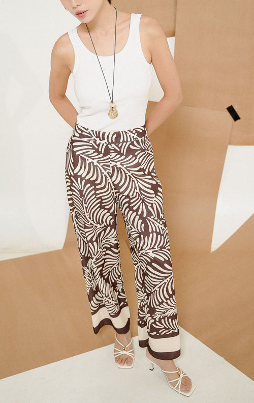 Model mengenakan Mckinney Pants Dark Brown, produk celana panjang kulot wanita potongan longgar warna cokelat tua dengan motif daun botanical tropis.
