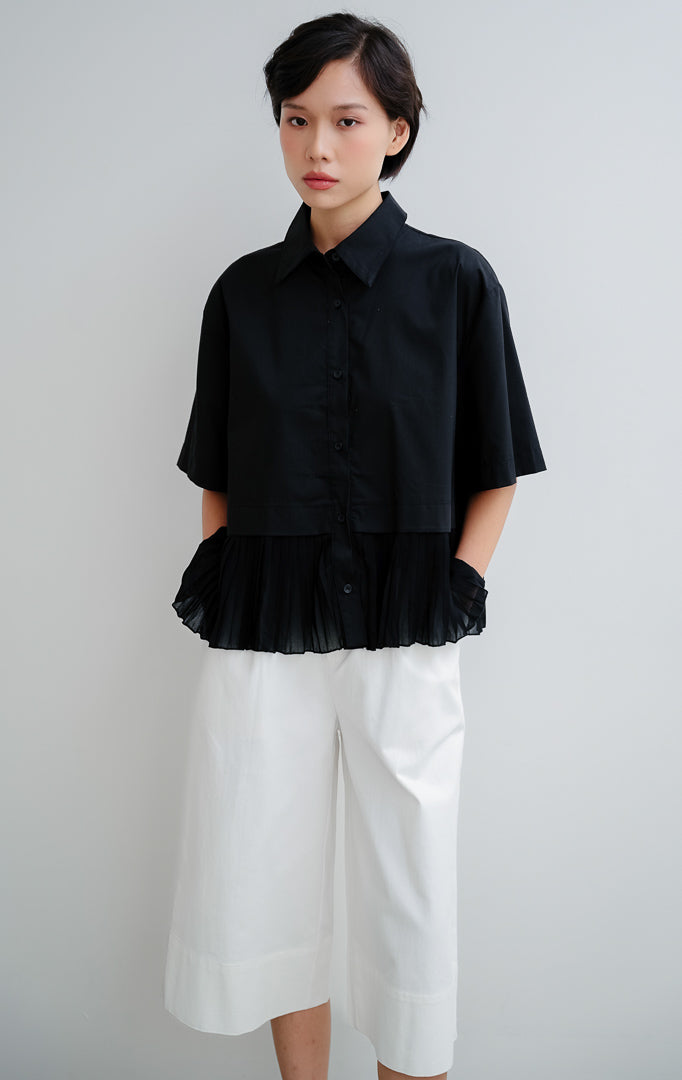Atasan blouse wanita warna hitam Mildred Top dengan detail lipit (pleats), siluet peplum yang anggun, kancing depan (button-up), dan bahan katun poliester.