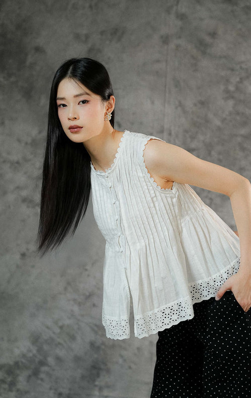 Blouse peplum tanpa lengan wanita Misty warna putih bersih berbahan katun dengan detail pintuck, kerah berhias lace bordir, dan keliman ruffle bawah. 