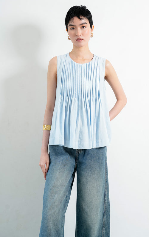Atasan wanita tanpa lengan warna biru muda (light blue sleeveless top) Miuza Top berbahan kain tenun ringan dengan detail panel plisket vertikal di bagian depan (vertical pleated panels), kerah bulat (round neckline), serta bagian bawah berkerut yang lembut (softly gathered lower section).
