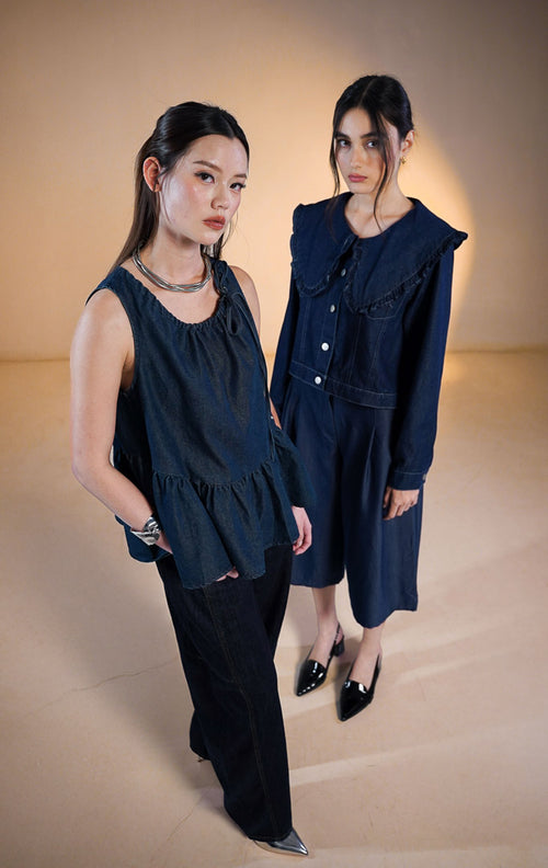 Model wanita mengenakan Mokpo Peter Pan Ruffle Collar Denim Top, atasan denim biru tua (dark wash) dengan kerah lebar model Peter Pan berenda (ruffle trim), kancing depan perak, dan jahitan kontras