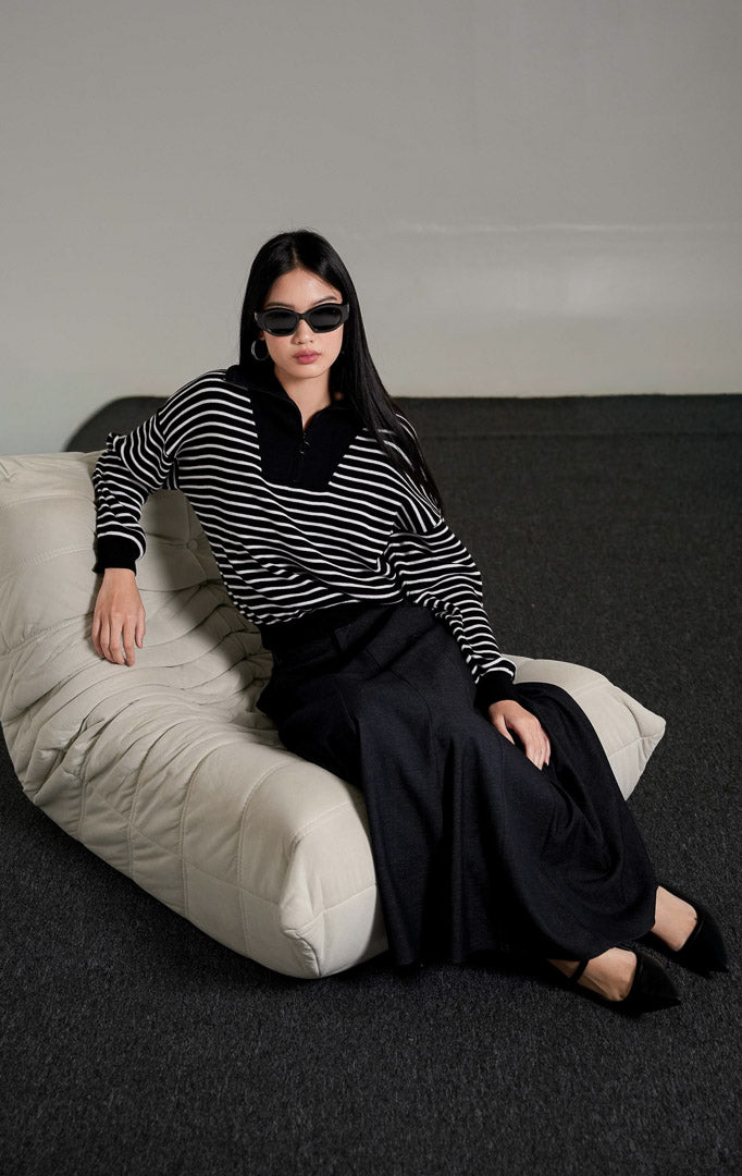Monette Collared Striped Sweater rajut motif garis hitam putih dengan kerah half-zip, dipadukan dengan rok panjang abu-abu gelap.
