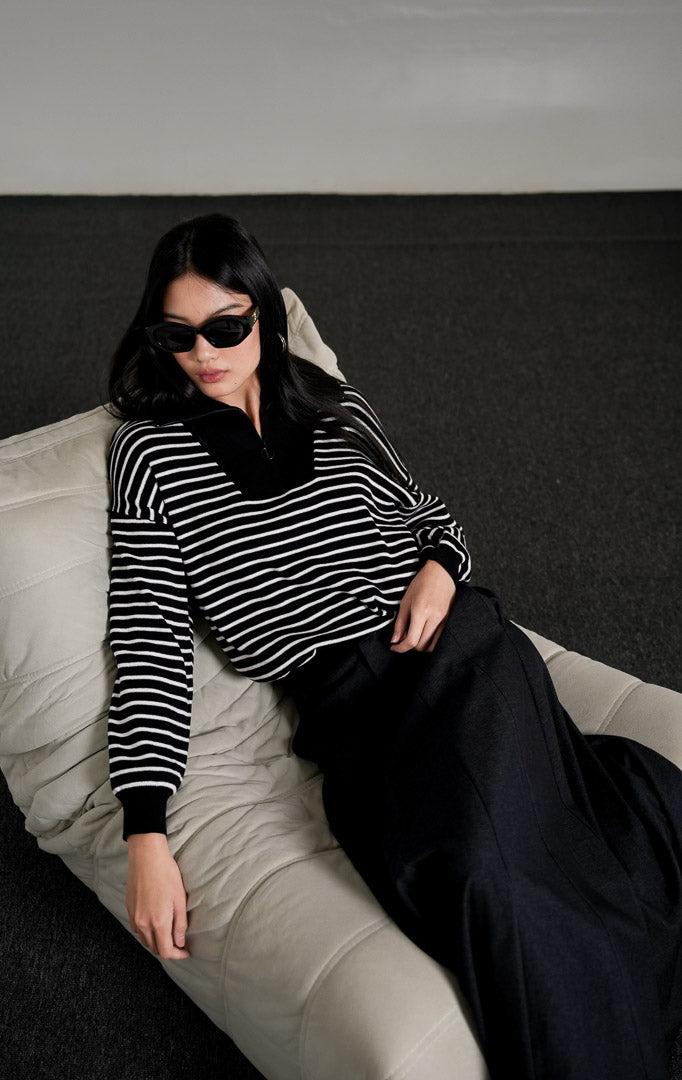 Monette Collared Striped Sweater rajut motif garis hitam putih dengan kerah half-zip, dipadukan dengan rok panjang abu-abu gelap.