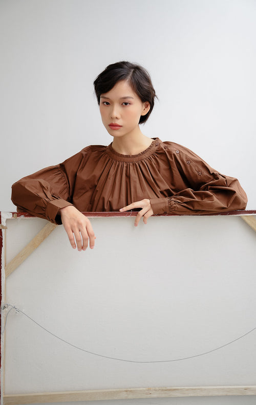 Atasan blouse wanita warna cokelat tua (dark brown) Morgana Top berbahan katun breathable dengan aksen kancing unik pada bagian bahu untuk gaya clean dan minimalist.
