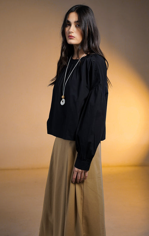 Model wanita mengenakan Morgana Puffy Sleeve Cropped Top warna hitam, atasan lengan panjang balon (puffy) dengan detail deretan kancing di sepanjang garis bahu hingga lengan, dipadukan dengan kalung panjang