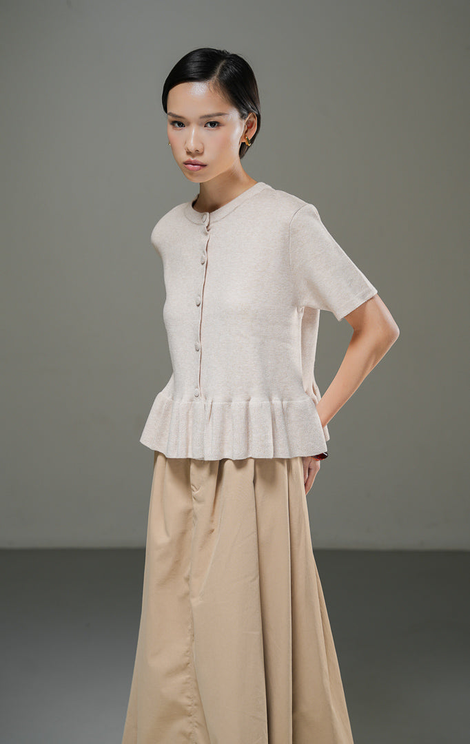 Atasan rajut wanita Naari Top Khaki lengan pendek dengan kerah bulat, kancing depan bungkus, dan detail rumbai (ruffle hem) rajut di bagian bawah. 