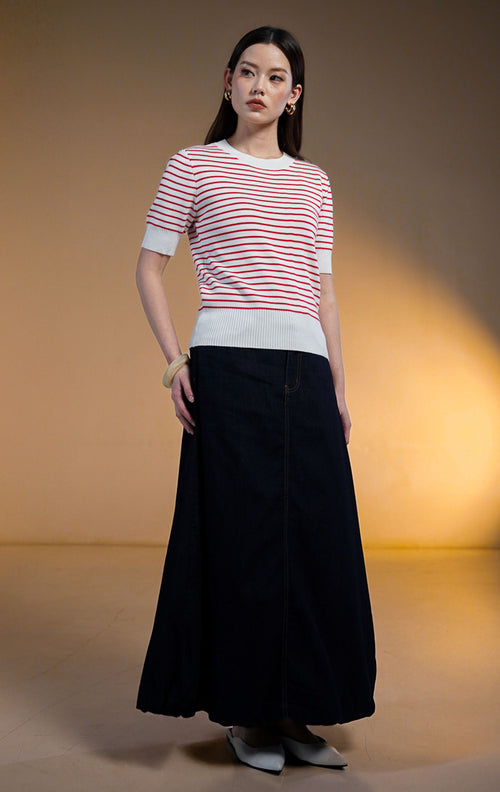 Model wanita mengenakan Naira Stripe Knit Top warna putih dengan garis garis merah (red stripes), atasan rajut lengan pendek dengan detail rib putih di leher dan lengan, dipadukan dengan rok denim gelap