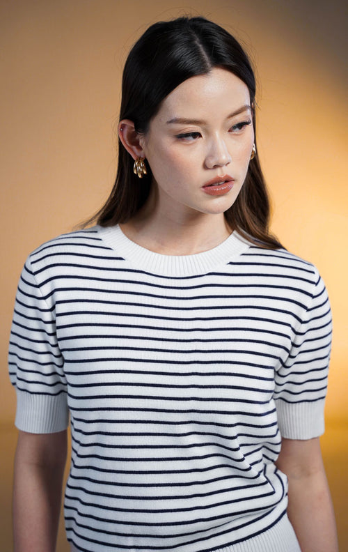 Model wanita mengenakan Naira Stripe Knit Top warna putih, atasan rajut lengan pendek dengan motif garis garis biru dongker (navy stripes), kerah bulat (crew neck) dengan trim rib putih