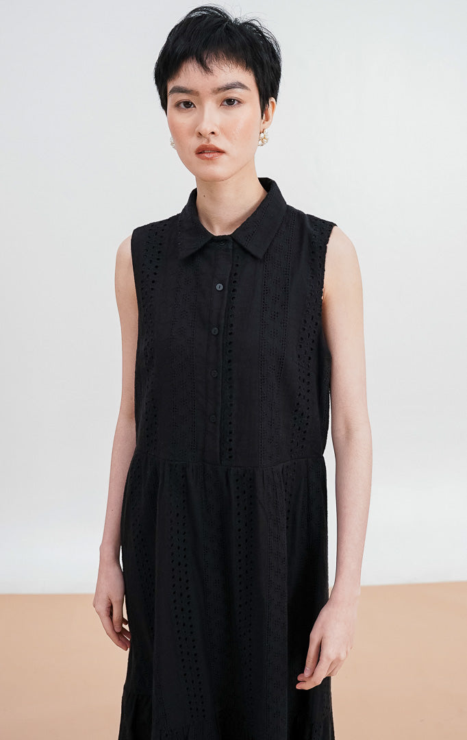 Model mengenakan Nalani Dress warna black, gaun maxi tanpa lengan dengan kerah kemeja, detail bordir eyelet di seluruh bagian, dan potongan bertingkat (tiered).
