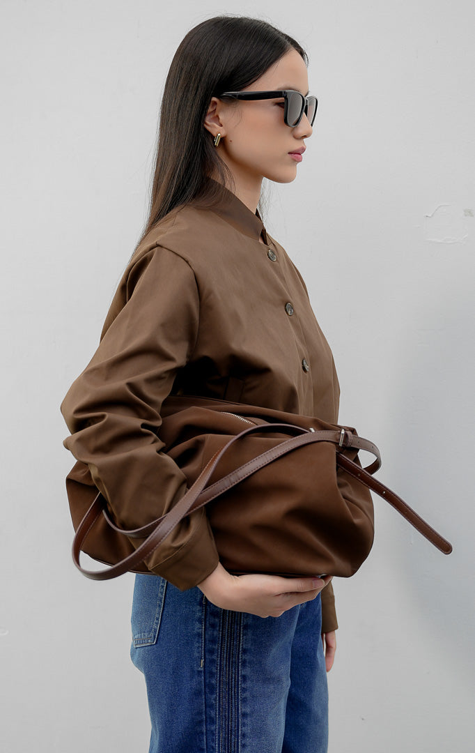 Jaket wanita model bomber tanpa kerah (collarless) warna cokelat tua (dark brown) Nicolette Jacket berbahan campuran katun-nilon dengan kancing depan dan saku samping fungsional.