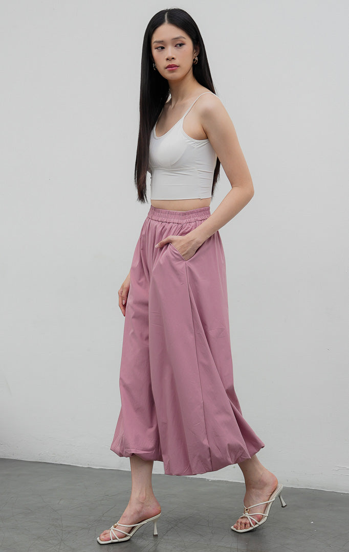 Celana panjang wanita model balon (balloon-leg pants) warna merah muda pudar (dusty pink) Nikolai Pants berbahan campuran katun nilon dengan detail kerut ujung celana (gathered hem) dan pinggang karet.
