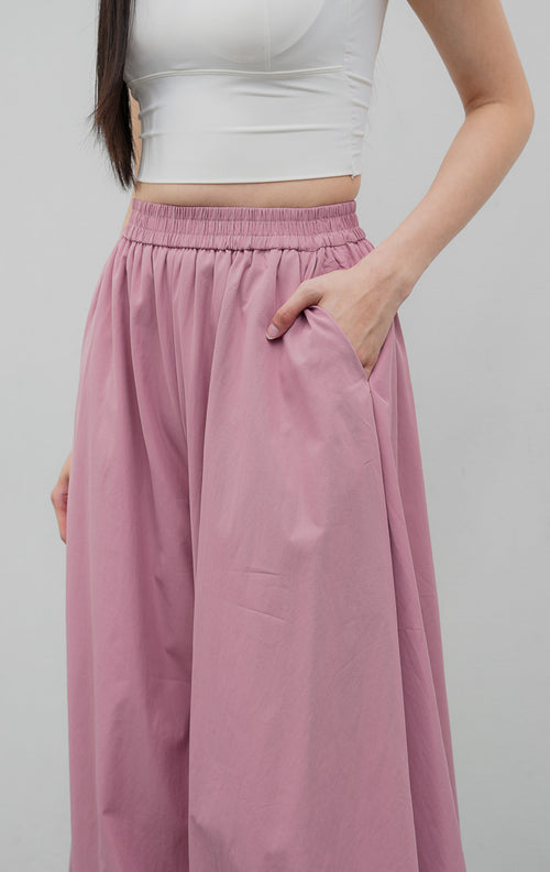 Celana panjang wanita model balon (balloon-leg pants) warna merah muda pudar (dusty pink) Nikolai Pants berbahan campuran katun nilon dengan detail kerut ujung celana (gathered hem) dan pinggang karet.