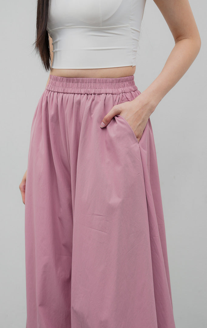 Celana panjang wanita model balon (balloon-leg pants) warna merah muda pudar (dusty pink) Nikolai Pants berbahan campuran katun nilon dengan detail kerut ujung celana (gathered hem) dan pinggang karet.