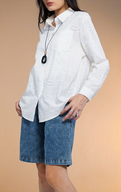 Model wanita mengenakan Nome Floral Embroidered Eyelet Shirt warna putih, kemeja lengan panjang kancing depan dengan motif bordir lubang (eyelet) dan saku dada, dipadukan dengan celana pendek denim dan sepatu boots putih