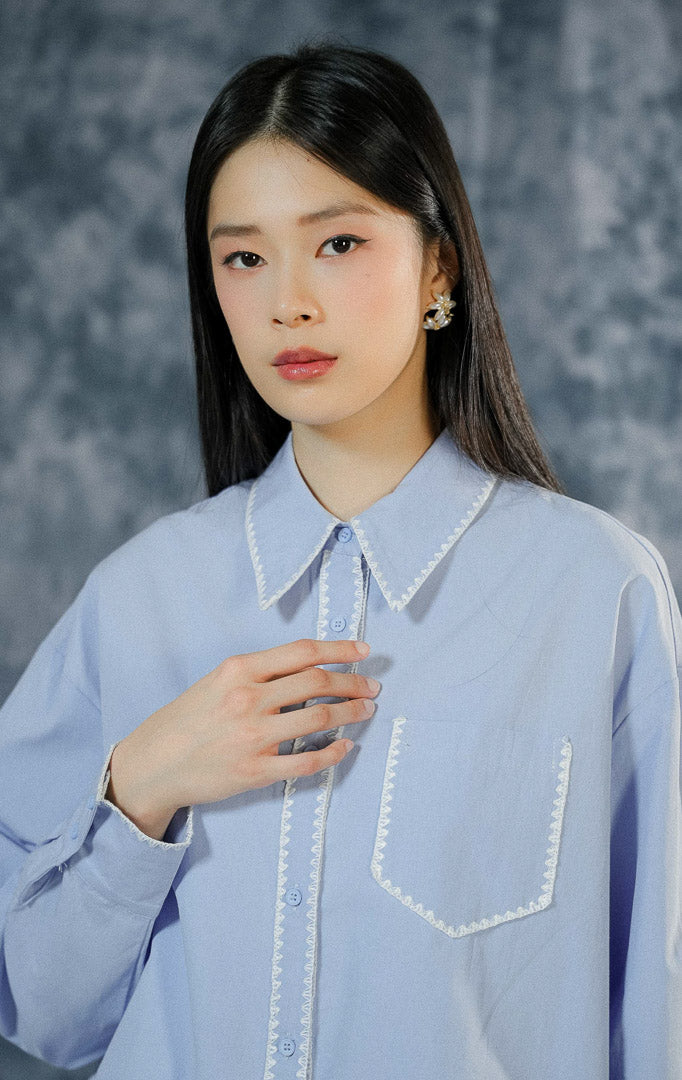 Kemeja lengan panjang wanita Nydia warna biru berbahan katun dengan detail motif sulam (embroidery) estetik di kerah, dilengkapi saku depan dan kancing aktif. 

