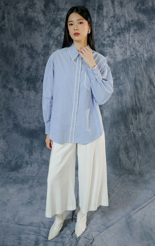 Kemeja lengan panjang wanita Nydia warna biru berbahan katun dengan detail motif sulam (embroidery) estetik di kerah, dilengkapi saku depan dan kancing aktif. 

