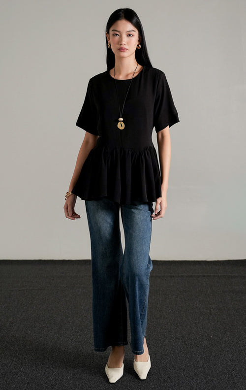 Nyla Top Black, atasan lengan pendek warna hitam dengan detail peplum lebar dan tali serut di pinggang, dipadukan dengan celana jeans flare.