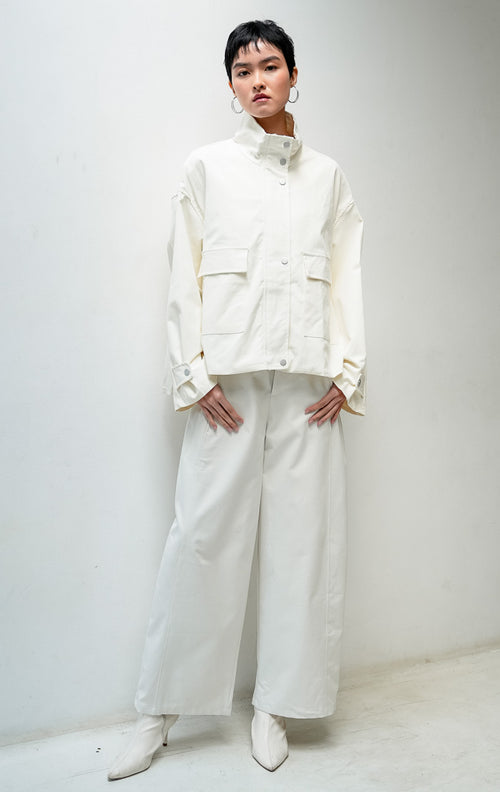 Jaket wanita lengan panjang warna ivory Octoviana Jacket dengan kerah tinggi (high neck), bukaan ritsleting dan kancing cetet (snap-button & zipper closure), saku kantong depan, serta detail lipit di bagian belakang (pleated back).