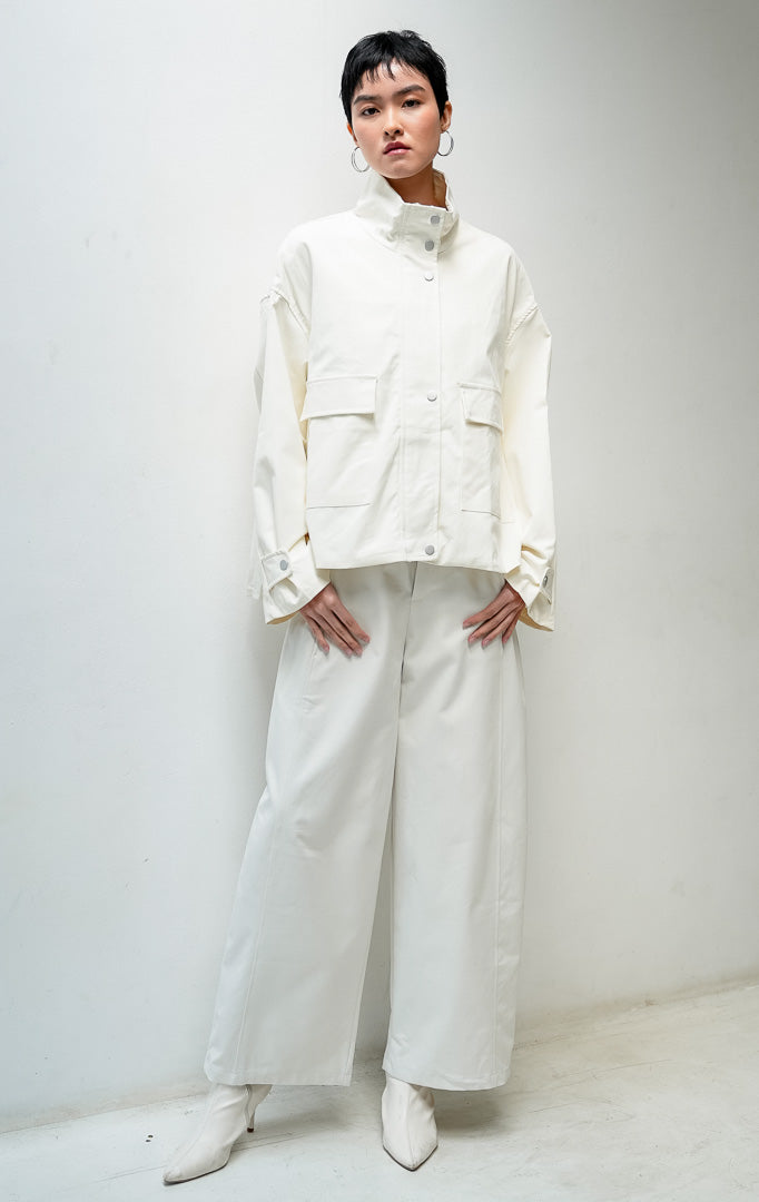 Jaket wanita lengan panjang warna ivory Octoviana Jacket dengan kerah tinggi (high neck), bukaan ritsleting dan kancing cetet (snap-button & zipper closure), saku kantong depan, serta detail lipit di bagian belakang (pleated back).