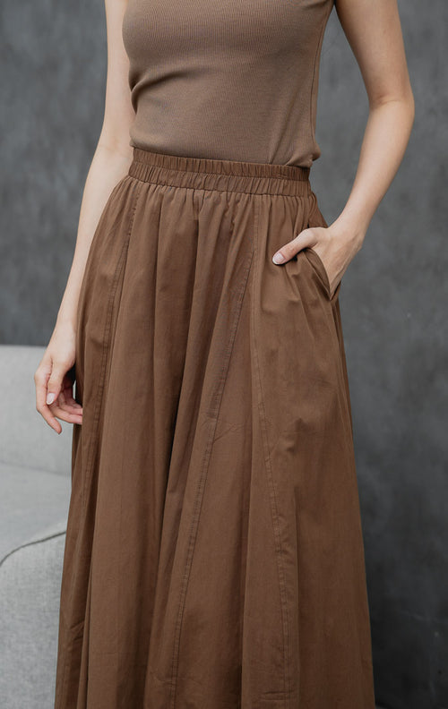 Rok maxi wanita model mekar (flared) warna cokelat tua (dark brown) Ophelia Skirt dengan detail jahitan panel, saku samping, dan pinggang full karet.