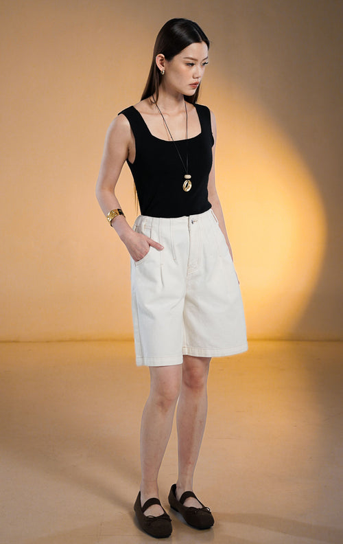 Model wanita mengenakan SH Ophira Short Denim Pants warna putih, celana pendek denim selutut (Bermuda) dengan pinggang karet dan saku samping, dipadukan dengan tank top hitam dan sepatu flat cokelat