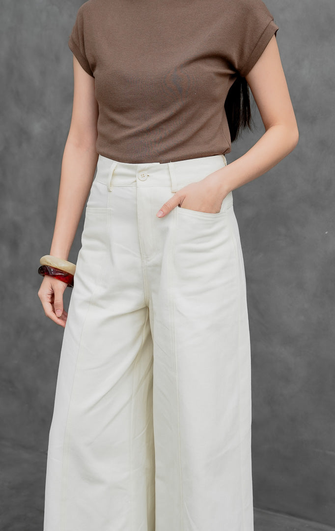 Celana panjang wanita model lebar (wide-leg pants) warna krem muda (ivory) Orian Pants berbahan cotton twill dengan jahitan panel melengkung (curved panel lines), saku utility depan, dan kancing resleting.