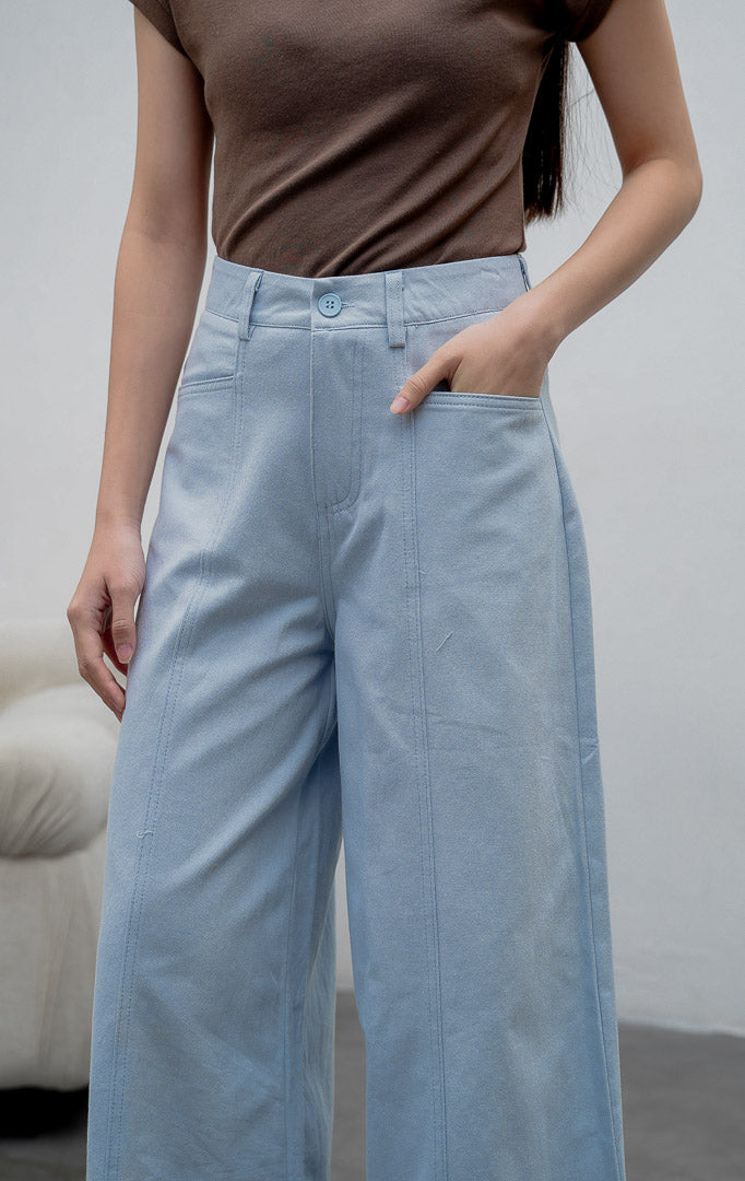 Celana panjang wanita model lebar (wide-leg pants) warna biru muda (light blue) Orian Pants berbahan cotton twill dengan jahitan panel melengkung (curved panel lines), saku utility depan, dan kancing resleting.