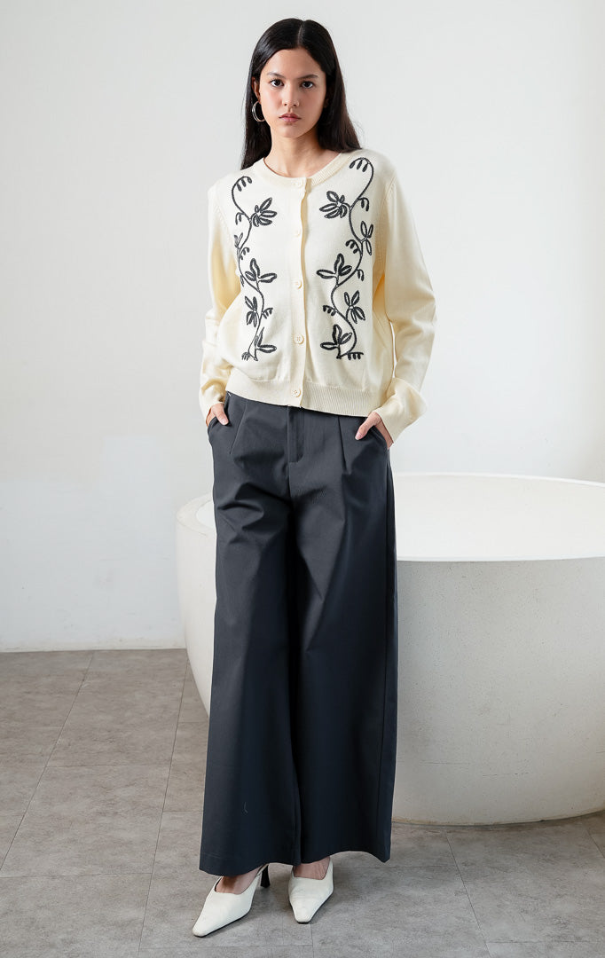Kardigan rajut wanita lengan panjang warna kuning muda (butter yellow) Oriana Cardigan berbahan soft knit dengan kerah bulat (rounded neckline), bukaan kancing depan, dan bordir motif sulur bunga warna kontras (contrasting floral vine embroidery). 