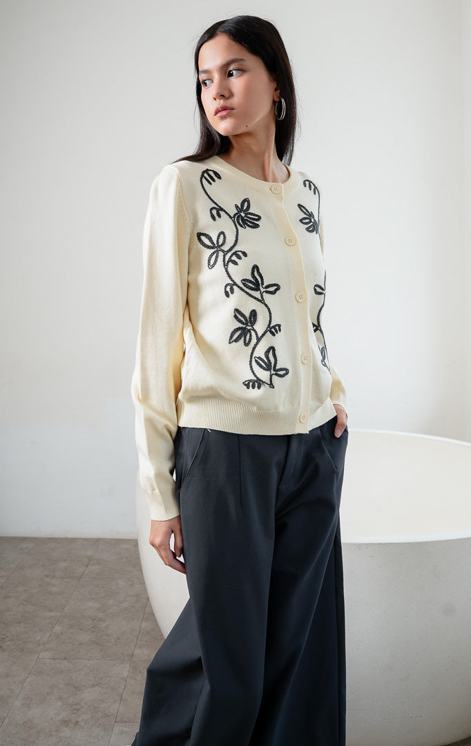 Kardigan rajut wanita lengan panjang warna kuning muda (butter yellow) Oriana Cardigan berbahan soft knit dengan kerah bulat (rounded neckline), bukaan kancing depan, dan bordir motif sulur bunga warna kontras (contrasting floral vine embroidery).