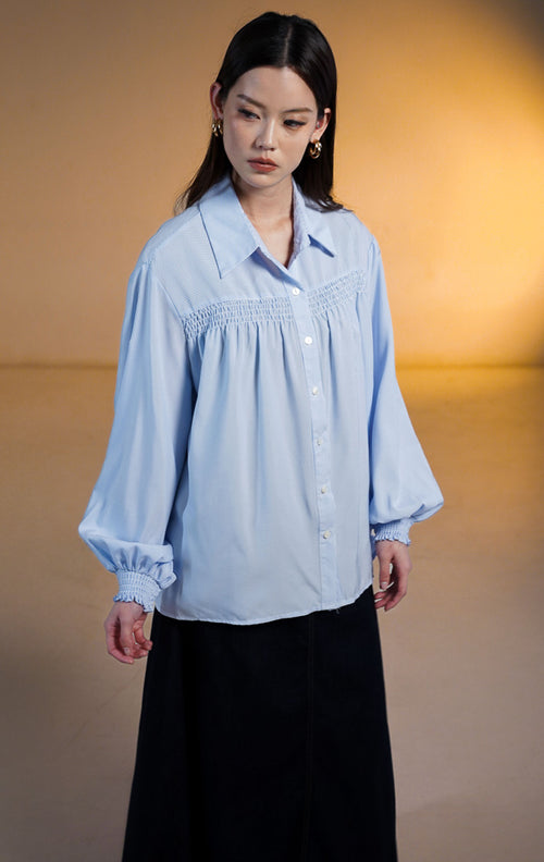 Wanita mengenakan kemeja biru Osiana Smocked Long Sleeve Shirt dengan detail kerutan di dada dan manset lengan panjang