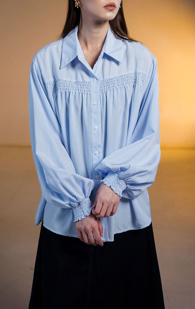 Wanita mengenakan kemeja biru Osiana Smocked Long Sleeve Shirt dengan detail kerutan di dada dan manset lengan panjang