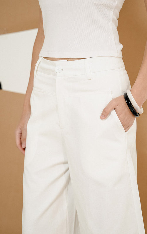 Model berdiri berpose mengenakan Paladia Soft Culottes Pants White, produk celana kulot wanita warna putih dengan potongan wide-leg tanggung dipadukan tank top putih. 