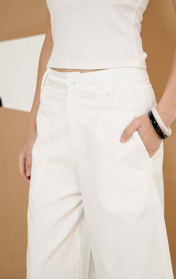 Model berdiri berpose mengenakan Paladia Soft Culottes Pants White, produk celana kulot wanita warna putih dengan potongan wide-leg tanggung dipadukan tank top putih. 