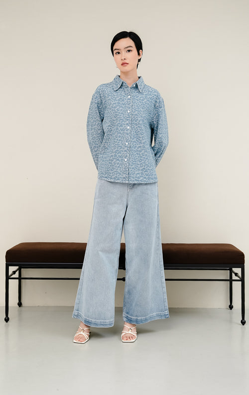Kemeja jeans wanita Panthera Top warna light denim biru muda dengan tekstur motif leopard jacquard, lengan panjang, dan kancing depan. 