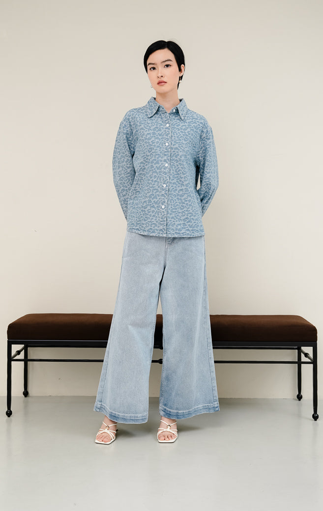 Kemeja jeans wanita Panthera Top warna light denim biru muda dengan tekstur motif leopard jacquard, lengan panjang, dan kancing depan. 