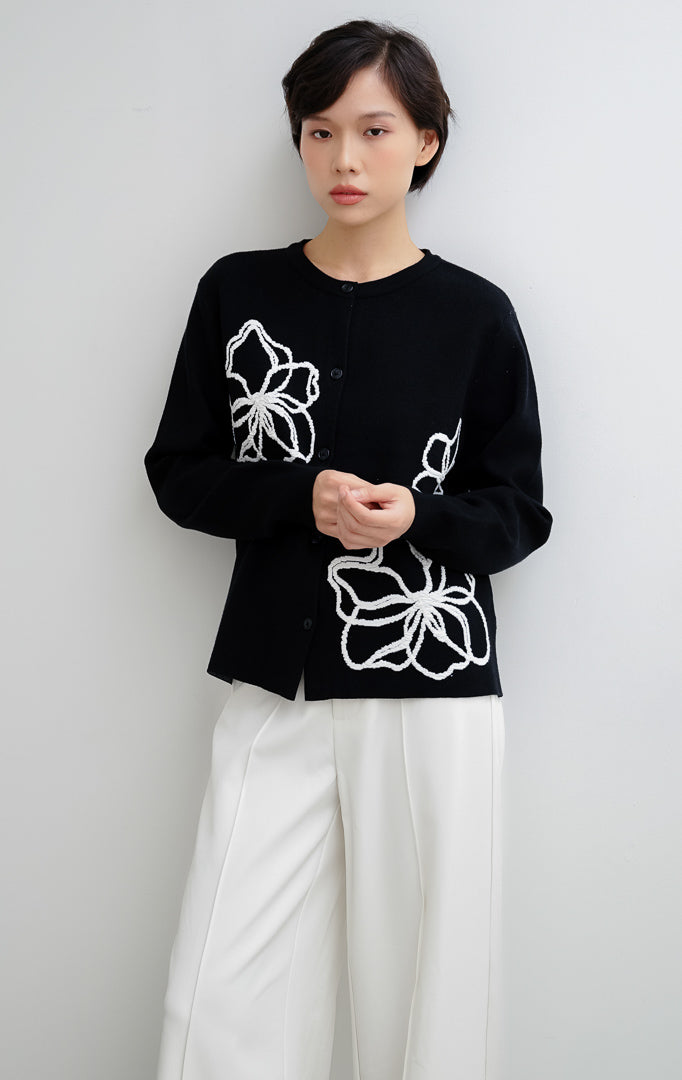Cardigan rajut wanita warna hitam Peppie Cardigan berbahan soft stretch dengan detail bordir bunga (flower embroidery) dan kancing depan (button-up).