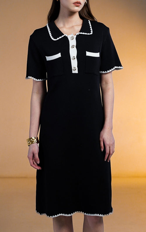 Model wanita mengenakan Perine Crochet Trim Mini Knit Dress warna hitam, gaun rajut lengan pendek dengan kerah dan saku dada bertepi renda putih (crochet trim) serta kancing depan emas.