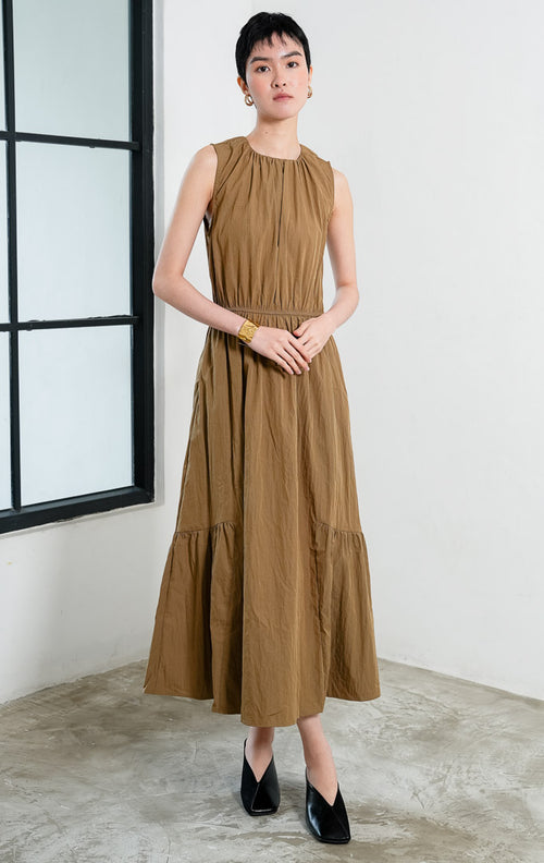 Gaun panjang wanita tanpa lengan (sleeveless maxi dress) warna cokelat muda (light brown) Persephone Dress berbahan crinkle ringan dengan aksen lipit leher (gathered neckline), pinggang karet elastis (elasticated waist), dan rok bertingkat (tiered skirt). 
