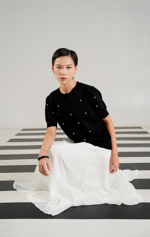 Atasan rajut lengan pendek wanita Polina Top Black dengan detail hiasan mutiara putih (pearls) yang tersebar di bagian depan, kerah bulat (crew neck), dan rib pada ujung lengan. 