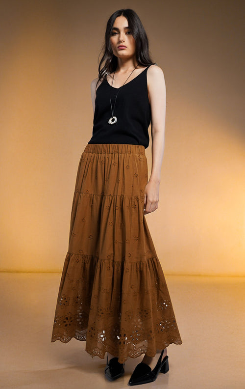 Model wanita mengenakan Primrose Tiered Midi Skirt warna cokelat, rok midi model susun (tiered) dengan bordir lubang bunga kecil (eyelet) dan pinggang karet, dipadukan dengan atasan tanpa lengan hitam