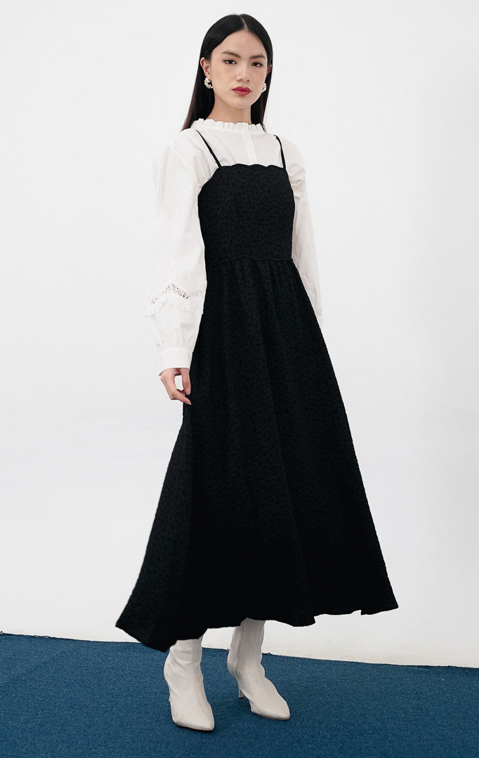  Model mengenakan Raelyn Dress warna black sebagai luaran, gaun maxi tali bahan jacquard tekstur bunga kecil dipadukan dengan kemeja Princeton putih di bagian dalam.