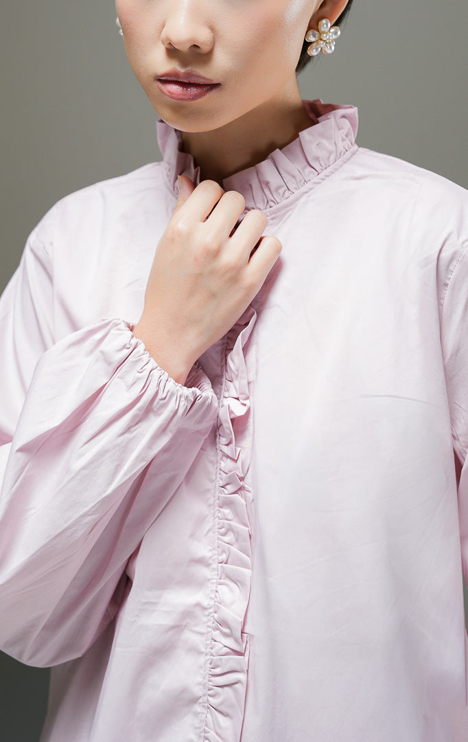Baju atasan wanita lengan panjang Raffaella Top warna dusty pink polos dengan detail kerah ruffle, aksen rumbai lipit di bagian bukaan kancing depan, dan ujung lengan berkaret. 