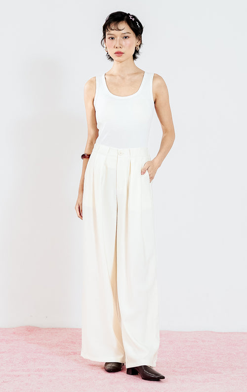 Celana panjang wanita Ramona Pants warna Ivory dari This Is April dengan detail lipit depan (pleats) dan potongan lurus, dipadukan dengan tank top putih.