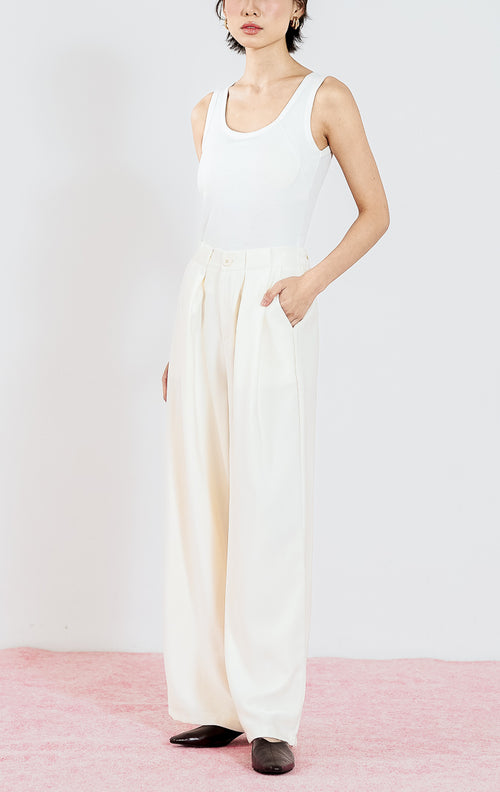 Celana panjang wanita Ramona Pants warna Ivory dari This Is April dengan detail lipit depan (pleats) dan potongan lurus, dipadukan dengan tank top putih.