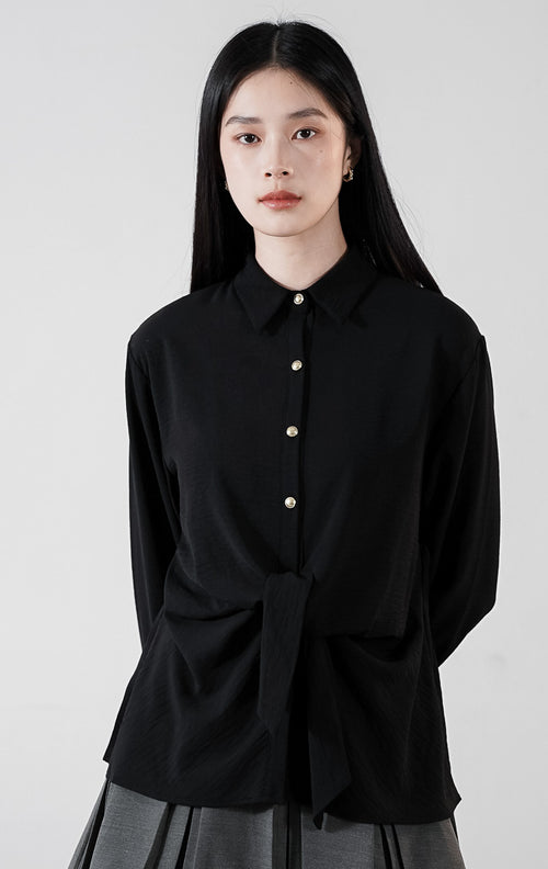 Raphina Top warna hitam, kemeja lengan panjang bertekstur crinkle dengan detail tali pita yang diikat di depan dan kancing emas kontras.1