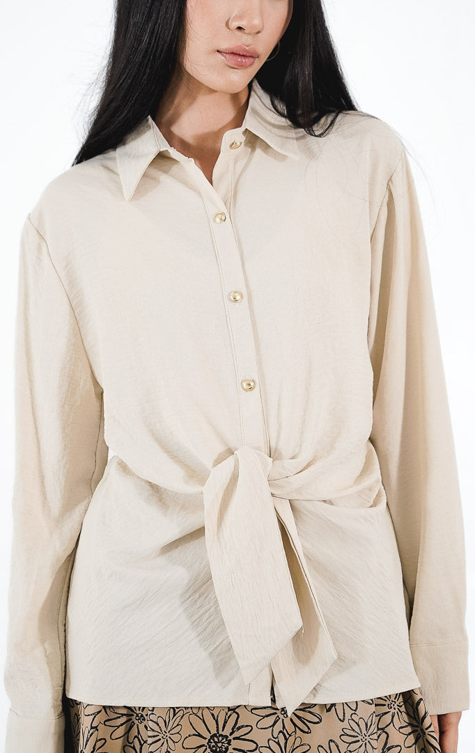 Raphina Top warna ivory, kemeja lengan panjang bertekstur crinkle dengan detail tali pita yang diikat di bagian pinggang dan kancing emas.1