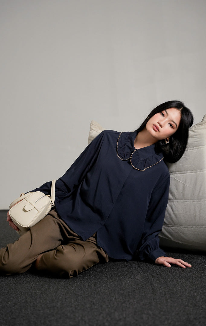 Rebecca Top Navy, kemeja katun lengan panjang warna biru tua (navy) dengan kerah scallop beraksen gelombang, dipadukan dengan celana bahan cokelat.
